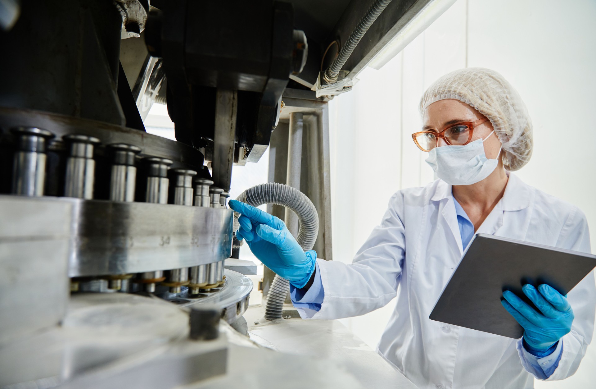 Process Technician in Gloves Inspecting Tablet Press at Pharmaceutical Manufacturing Plant